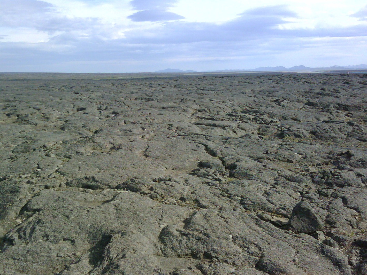 Rough grey Ódáðahraun lava stretching toward distant highland mountains.