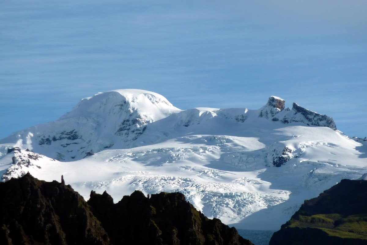 Öræfajökull rising above dark ridges and green lowland slopes in southeast Iceland.
