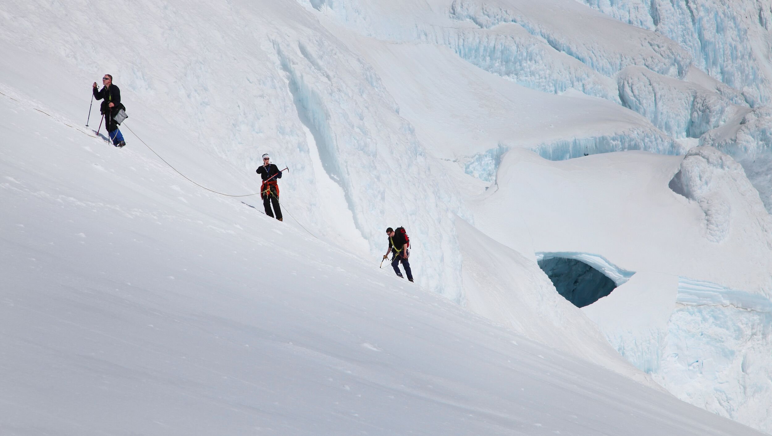 Roped climbers crossing snowy Öræfajökull terrain below blue ice walls.