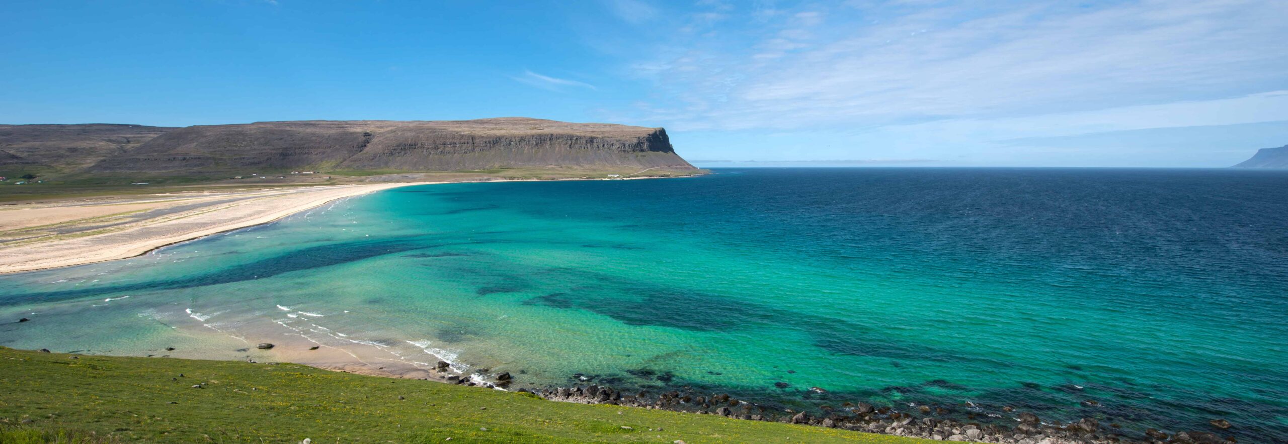 Orlygshofn Beach with pale sand, turquoise water, and broad Westfjords cliffs above the shoreline.