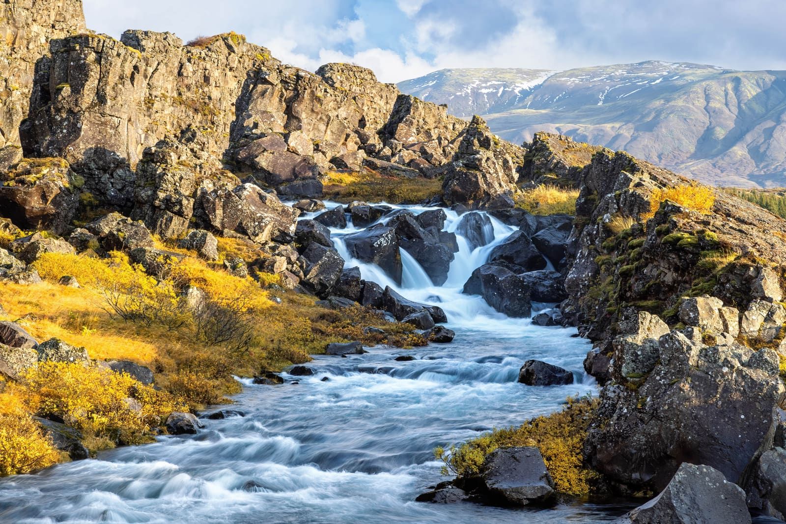 Öxará river running toward Öxarárfoss between dark rocks and autumn-colored brush in Þingvellir.
