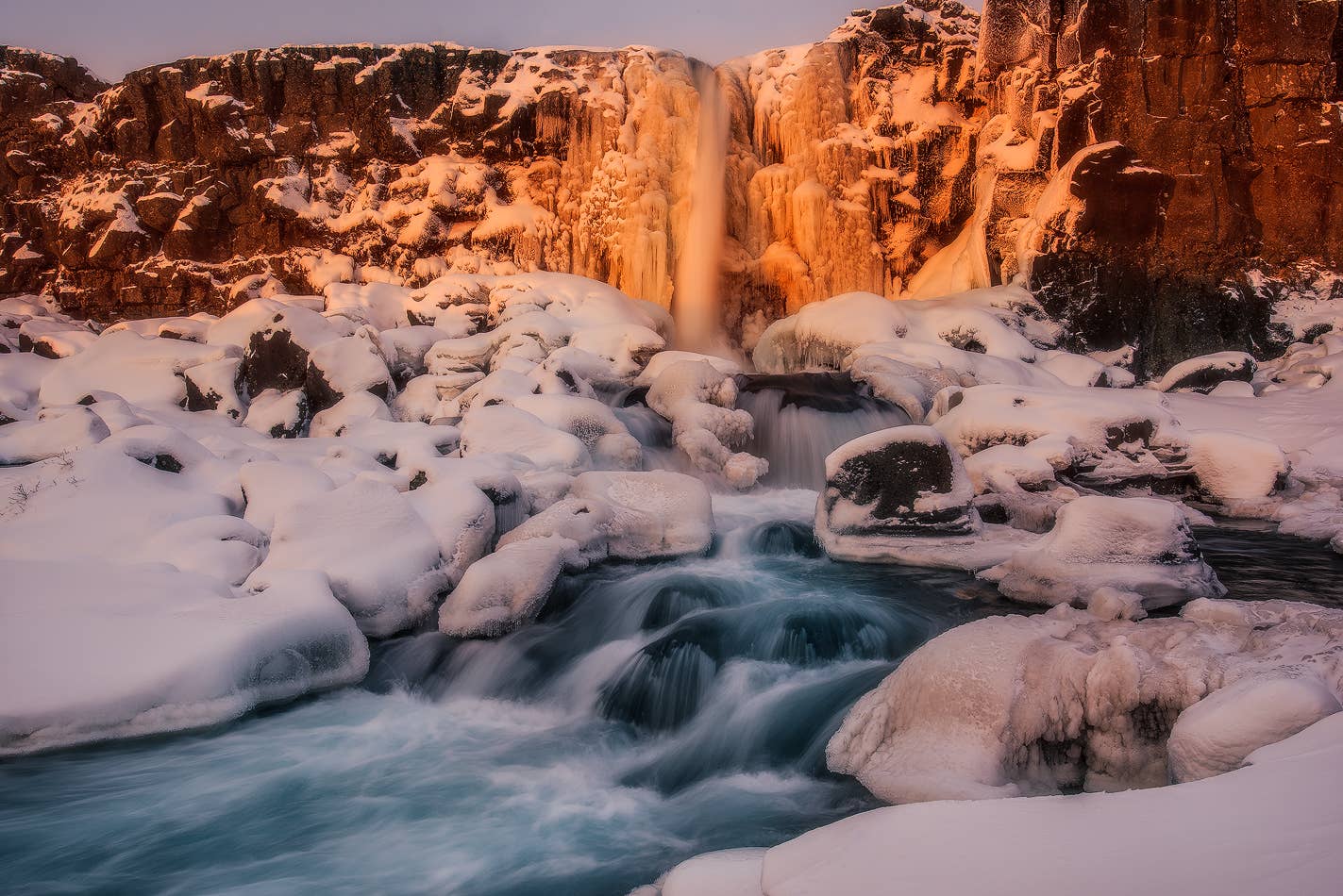Öxarárfoss in winter with snow and ice around the rocks below the falls.