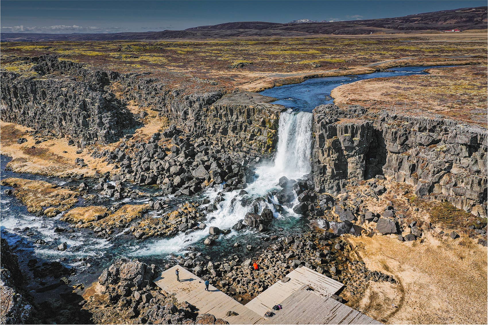 Aerial view of Öxarárfoss dropping into a rocky river channel with viewing platforms in Þingvellir.