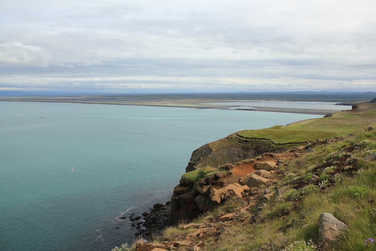 View from Hringsbjarg over Öxarfjörður, black-sand coast, and pale blue water.