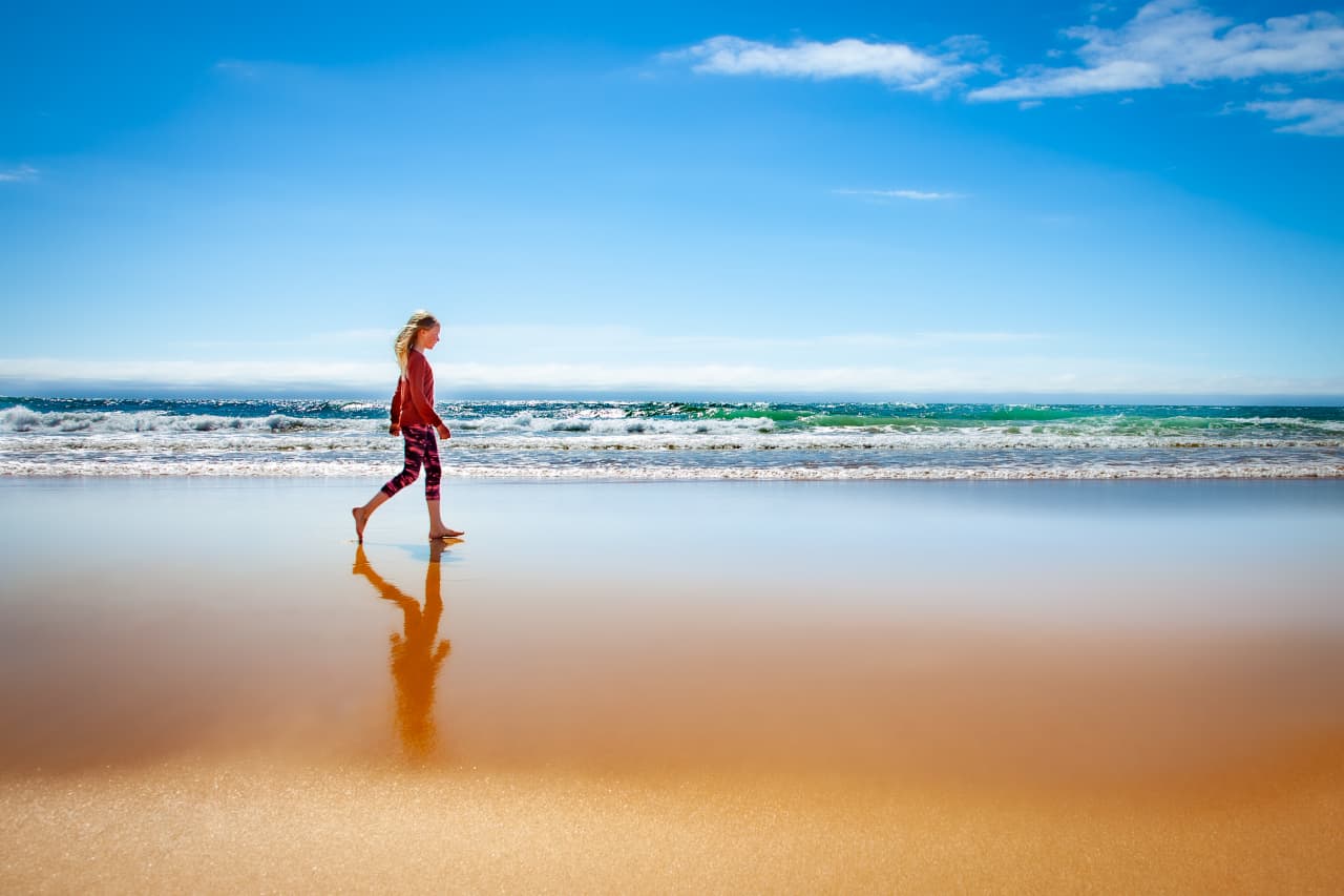 A person walking along the wet red-gold shoreline at Rauðasandur Beach with waves behind them.
