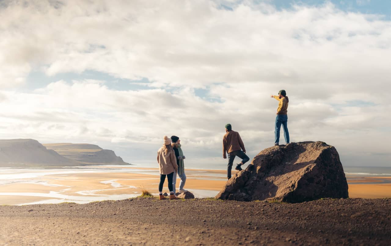 Travelers looking across Rauðasandur Beach from a rocky viewpoint above red-gold tidal flats.