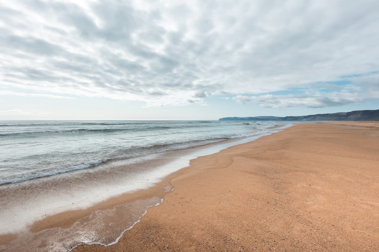 A broad quiet view across Rauðasandur Beach with red-gold sand, shallow water, and Westfjords cliffs.