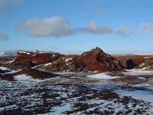 Snow patches and red Rauðhólar slopes under a clear sky near Reykjavík.