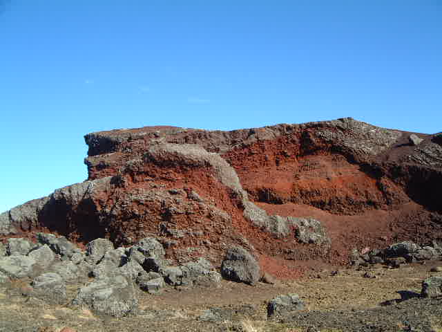 Close red Rauðhólar crater wall with dark lava rock and bare ground.