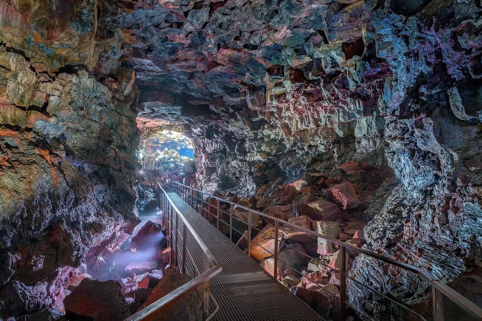 Metal walkway leading through the illuminated basalt passage inside Raufarhólshellir lava tunnel.