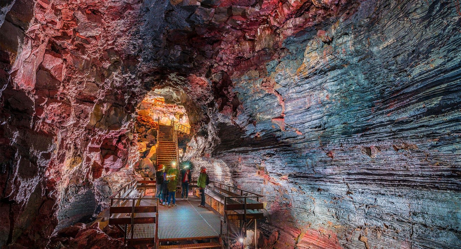 Visitors on a lit platform inside the colorful basalt passage of Raufarhólshellir lava tunnel.