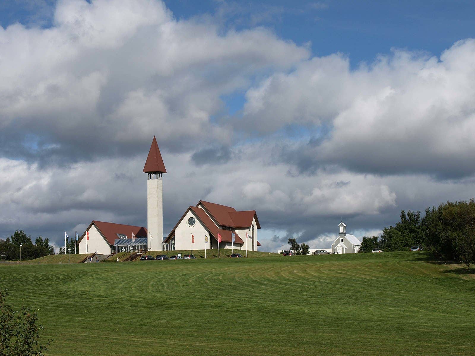 Reykholt churches and Snorrastofa buildings across a green field under broad clouds