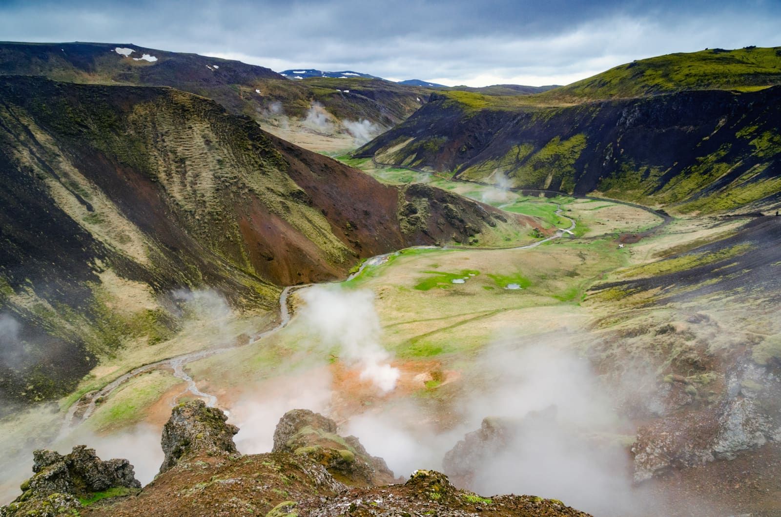 Steam rising from the green and dark slopes of Reykjadalur valley.