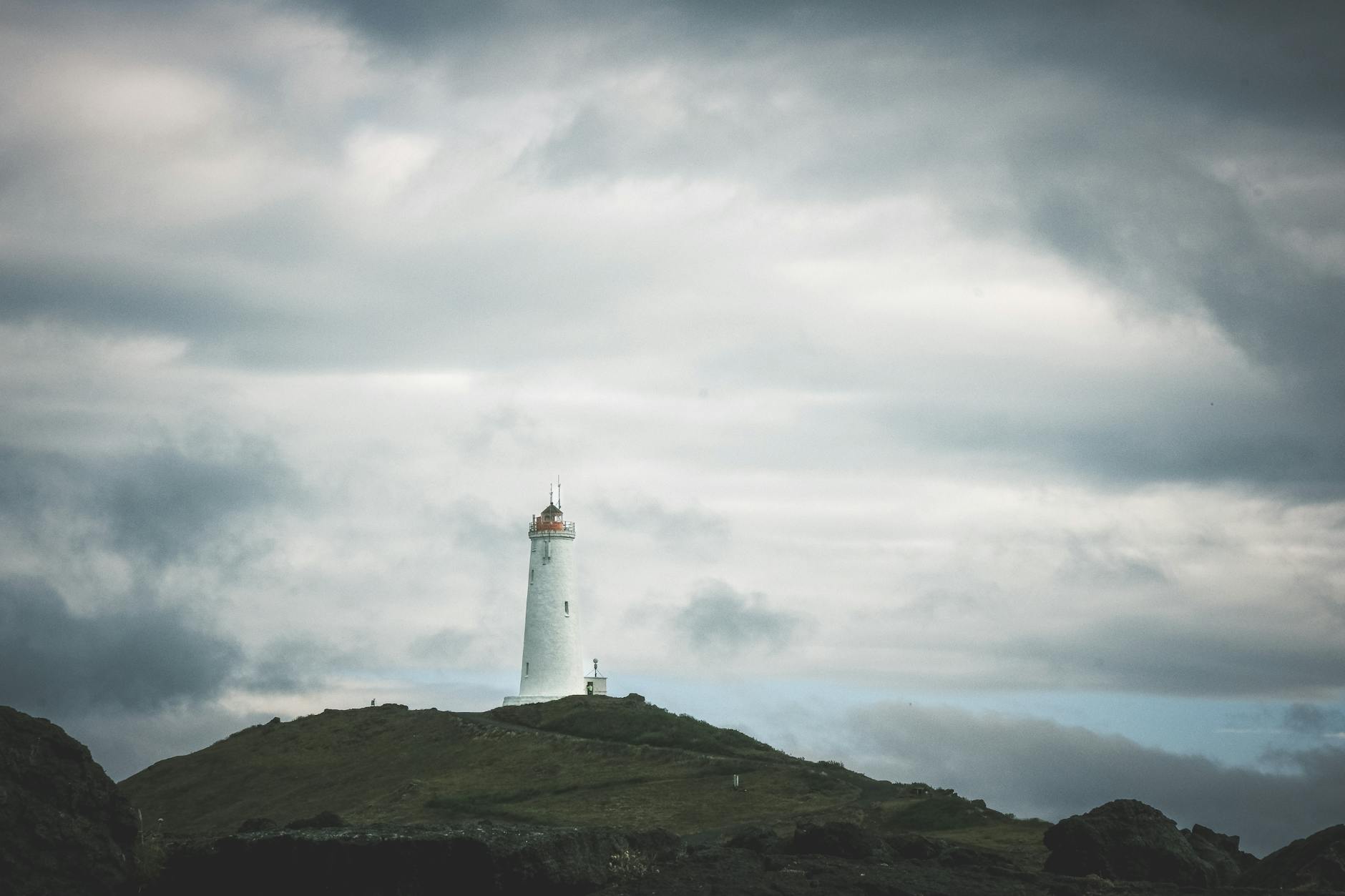 Reykjanesviti Lighthouse seen from across dark rocks under a moody overcast sky.