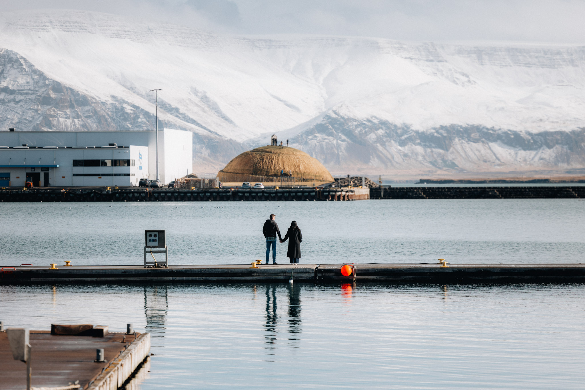 People on a Reykjavík harbour pier with Þúfa and snowy mountains beyond the water