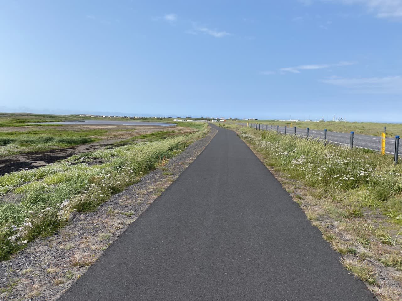 Paved coastal path leading toward Rif with wetlands on one side and the village in the distance.