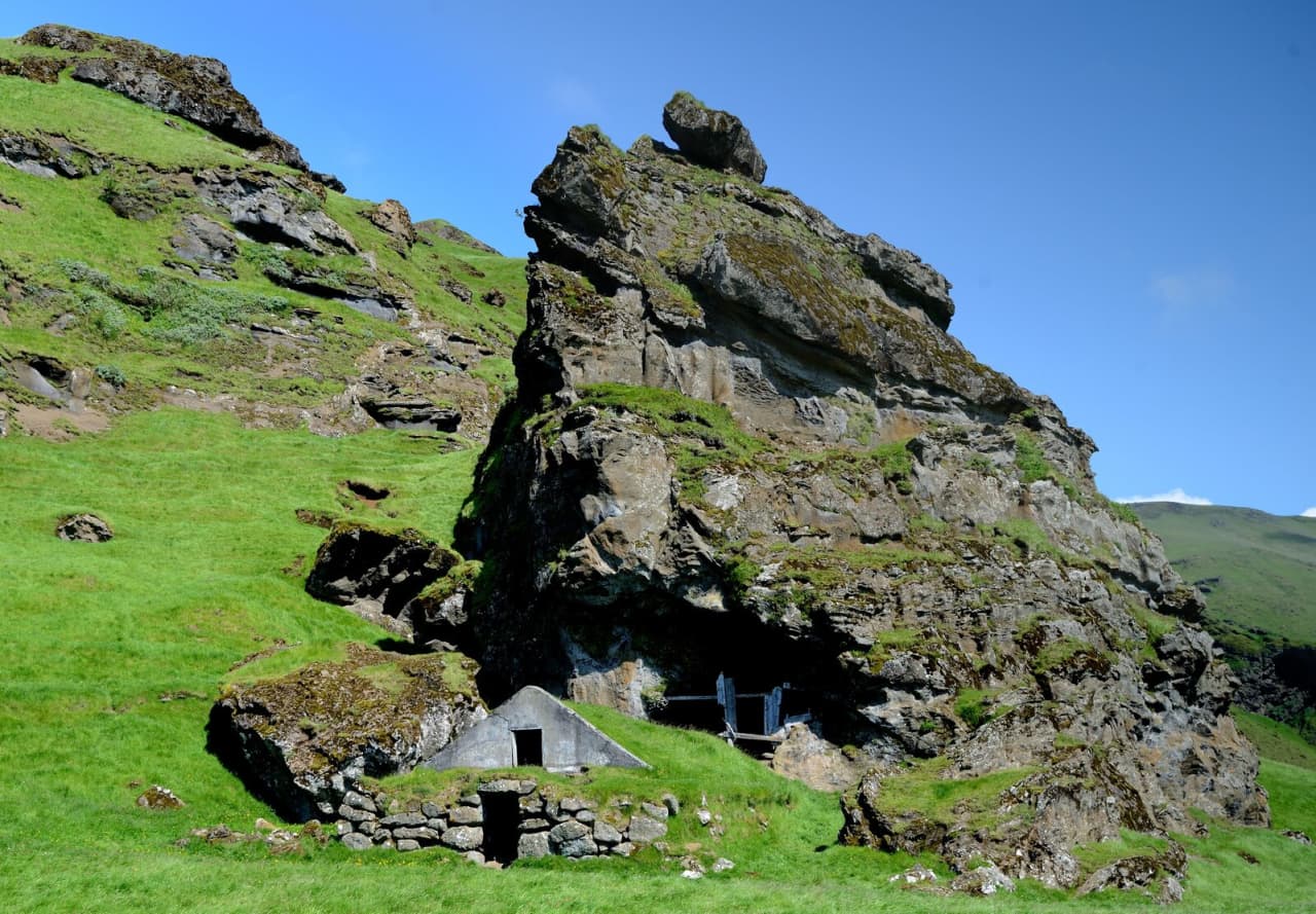 Rútshellir cave and its turf-fronted entrance beneath a broad green cliff under Eyjafjöll.