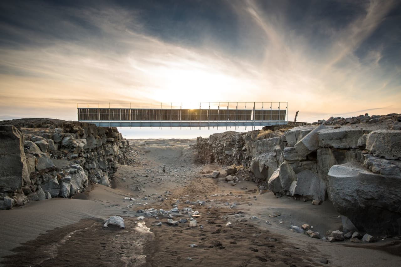 Bridge Between Continents spanning a sandy lava fissure near Sandvík under dramatic Reykjanes sky.