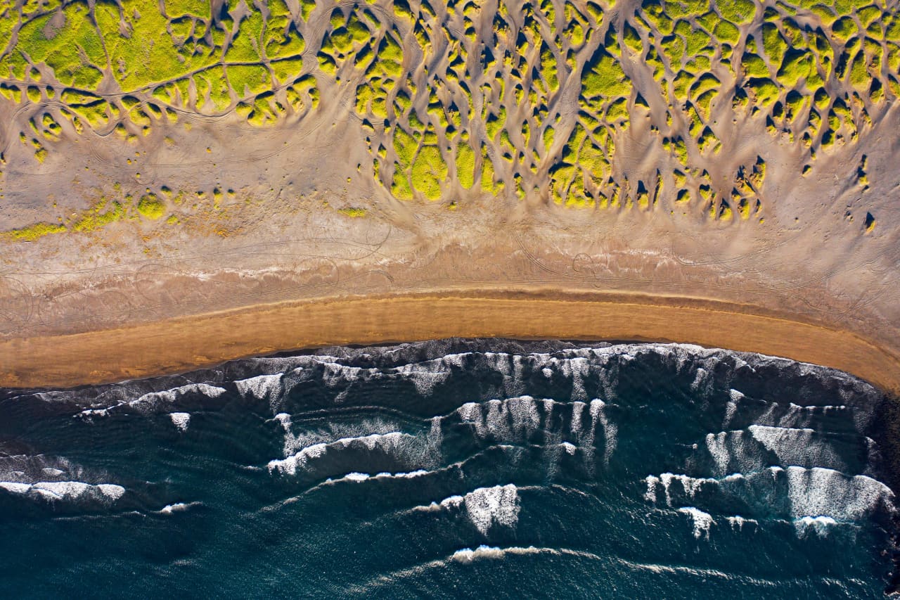 Black sand, surf, and grassy dune mounds at Sandvík on the Reykjanes Peninsula.