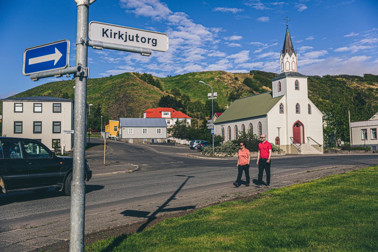 Kirkjutorg street sign, Sauðárkrókskirkja church, houses, and green hills in Sauðárkrókur.
