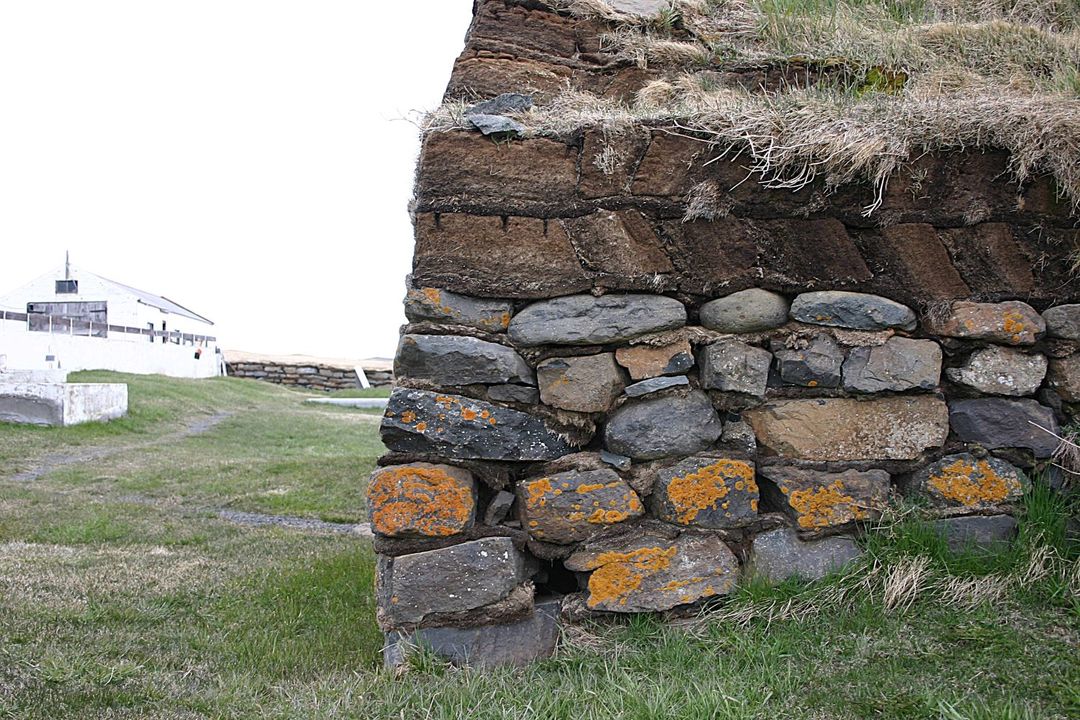 Close view of Saurbæjarkirkja stone wall, stacked turf, grass roof edge, and lichen-covered rocks.