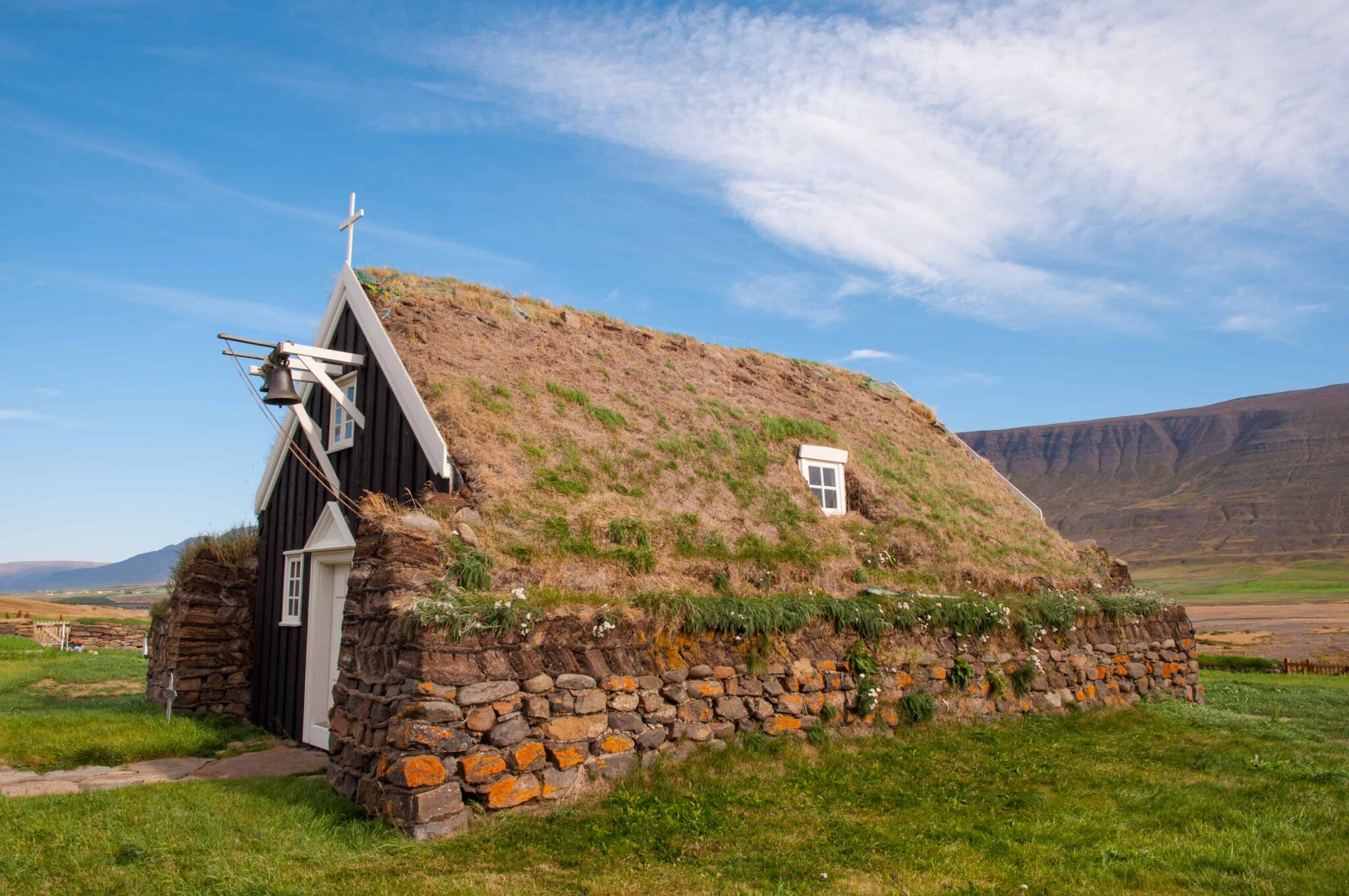 Saurbæjarkirkja turf church seen from the side with a grass roof, black gable, and open Eyjafjörður valley around it.