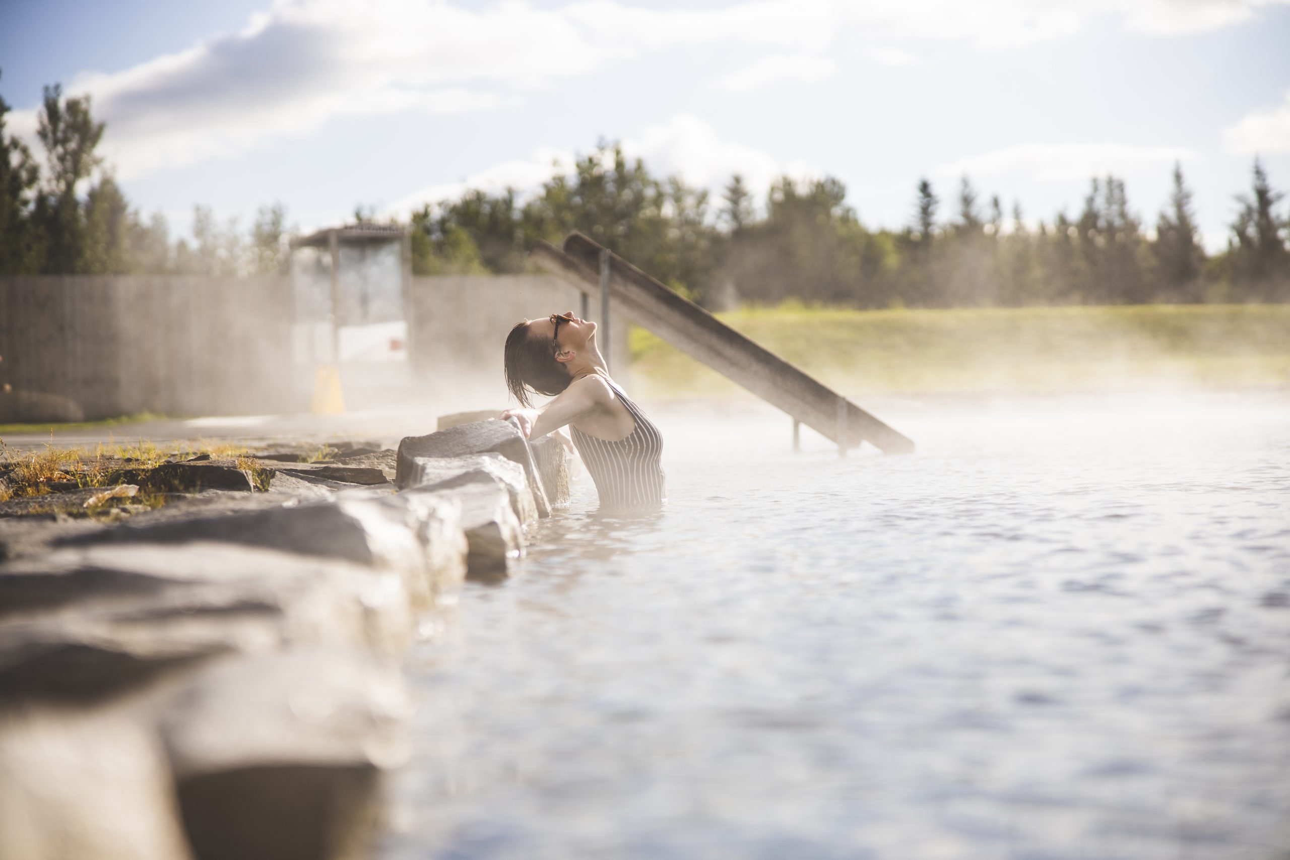 Visitor leaning back in the warm Secret Lagoon water with steam drifting across the pool edge.