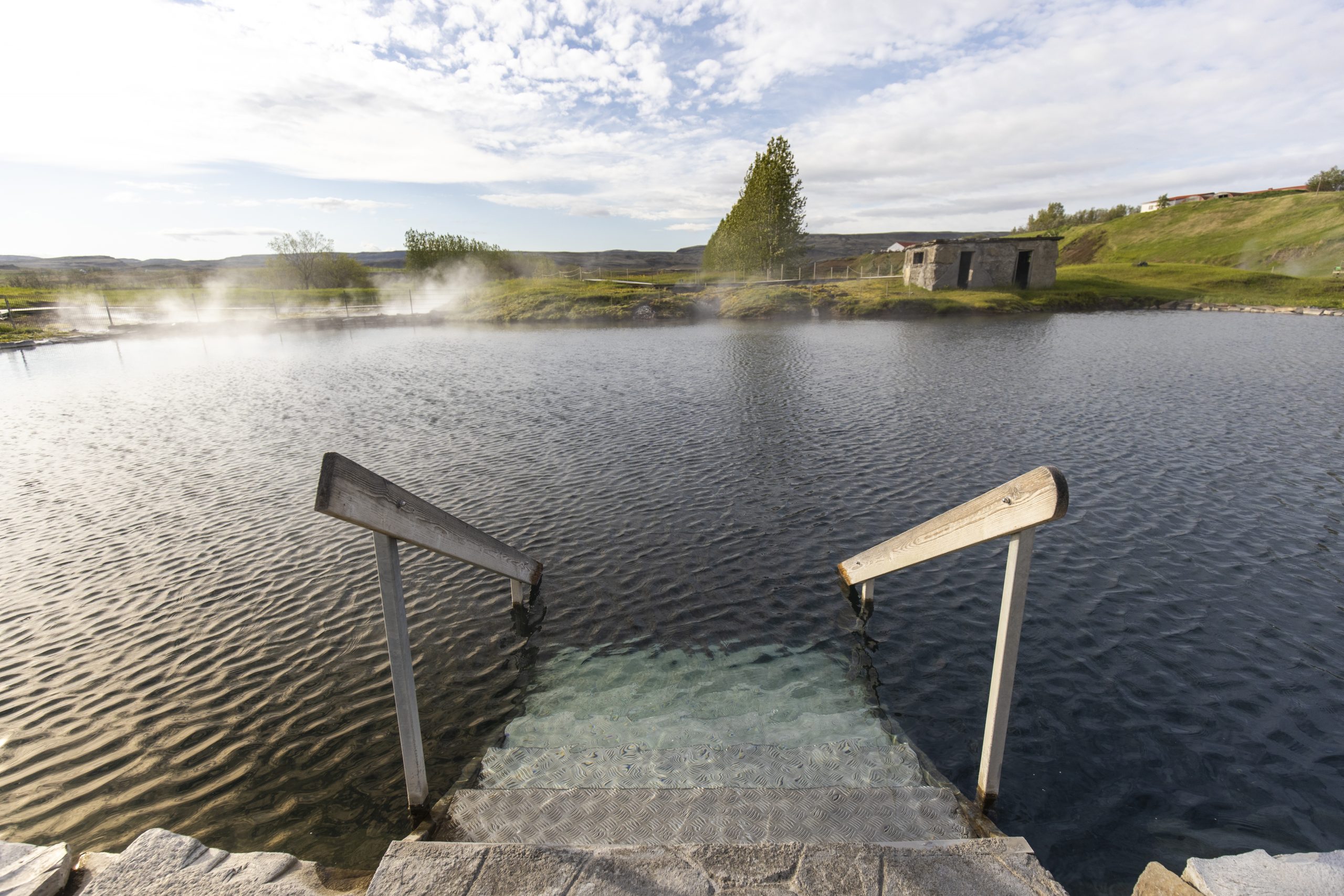Empty pool steps at Secret Lagoon with steam rising from the surrounding geothermal area.