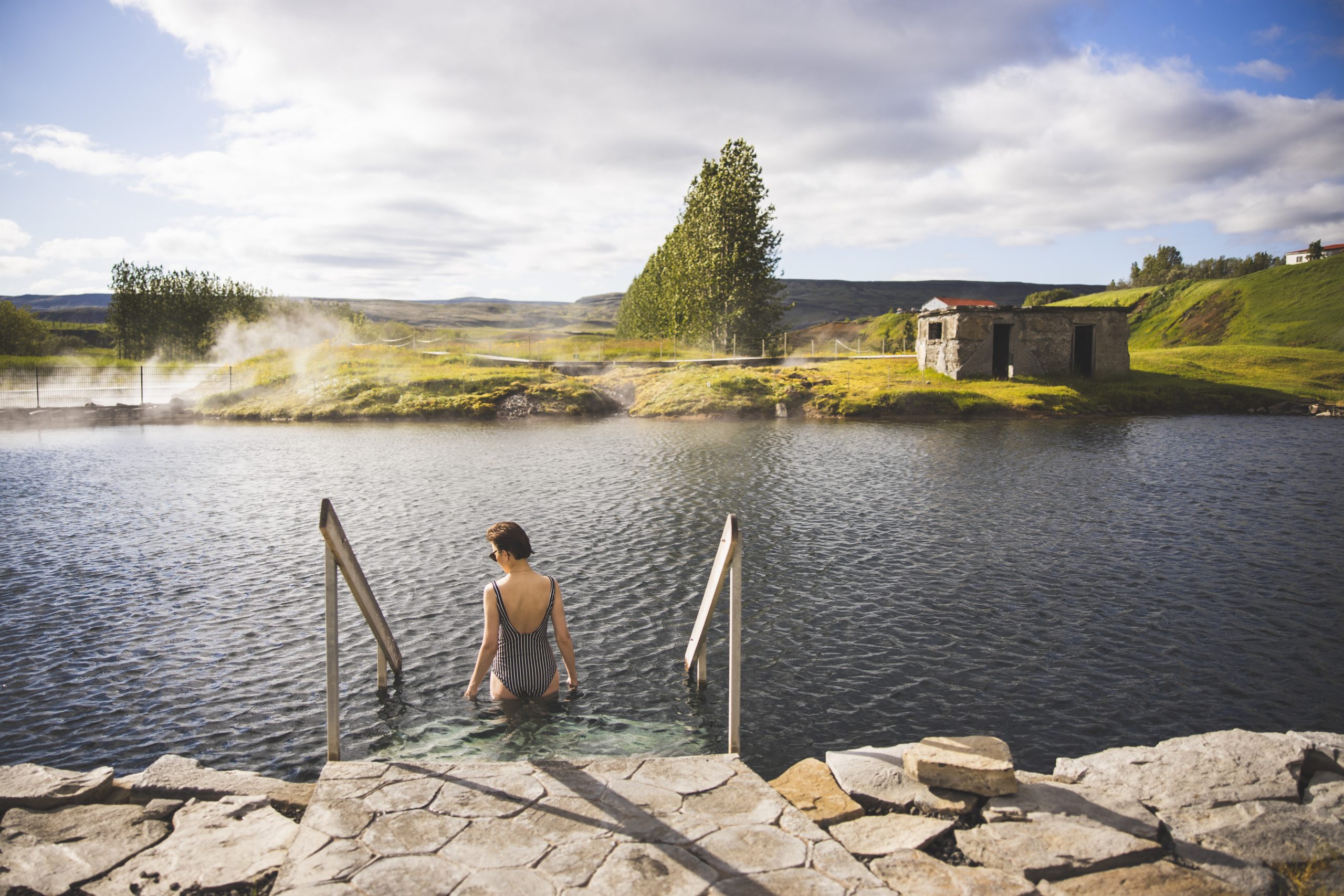 Bather entering the Secret Lagoon pool with steam rising around the old geothermal setting near Flúðir.