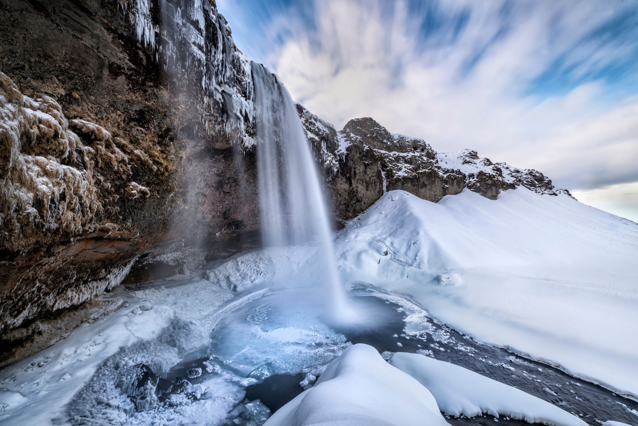 Seljalandsfoss flowing beside snow and ice in winter.