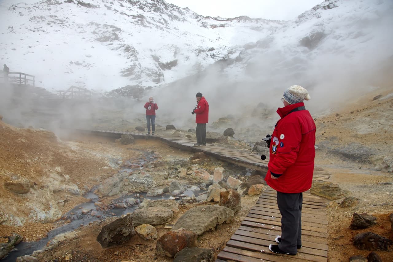 Visitors standing on the marked boardwalk through steam at Seltún geothermal area.