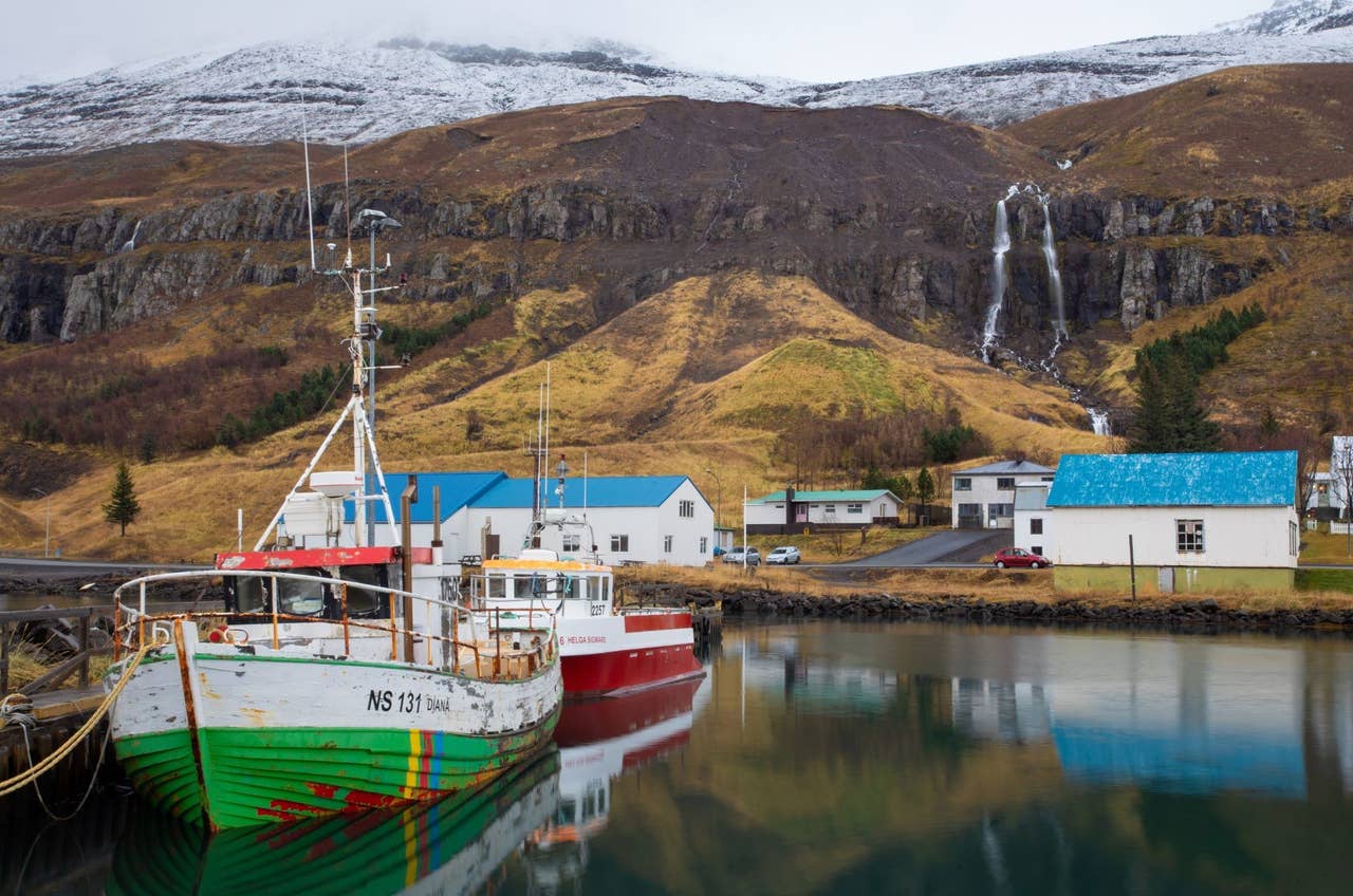 Fishing boats in Seyðisfjörður harbor with waterfalls and mountains behind the Eastfjords town.