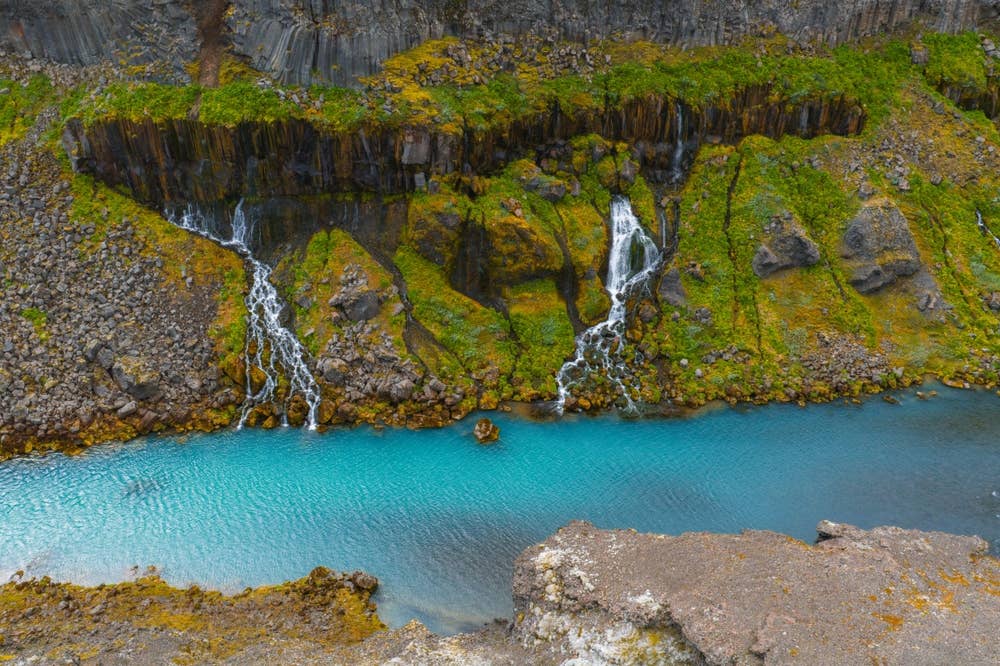 Turquoise water under mossy basalt cliffs in Sigöldugljúfur canyon.