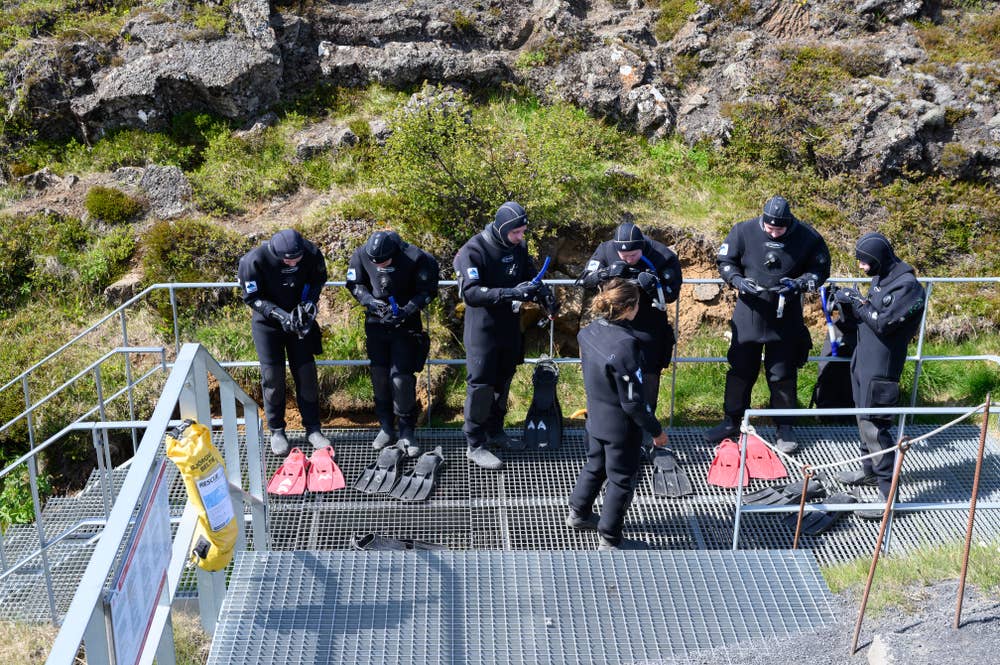 Snorkelers in dry suits preparing beside the Silfra entry platform in Þingvellir National Park.