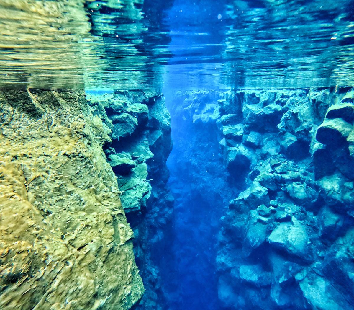 Underwater view through Silfra fissure with blue clear water and layered lava rock walls.