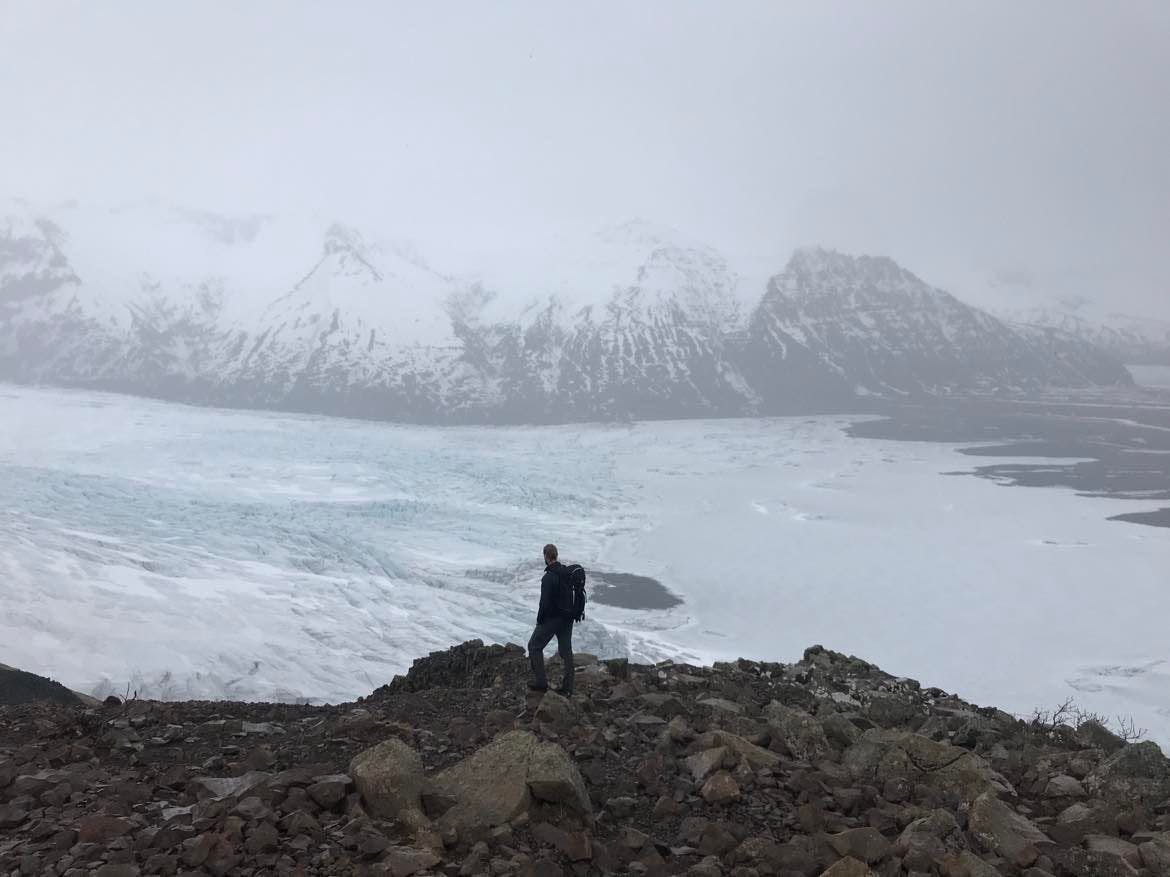 Hiker looking over a snowy glacier view from Sjónarnípa in the Skaftafell area.