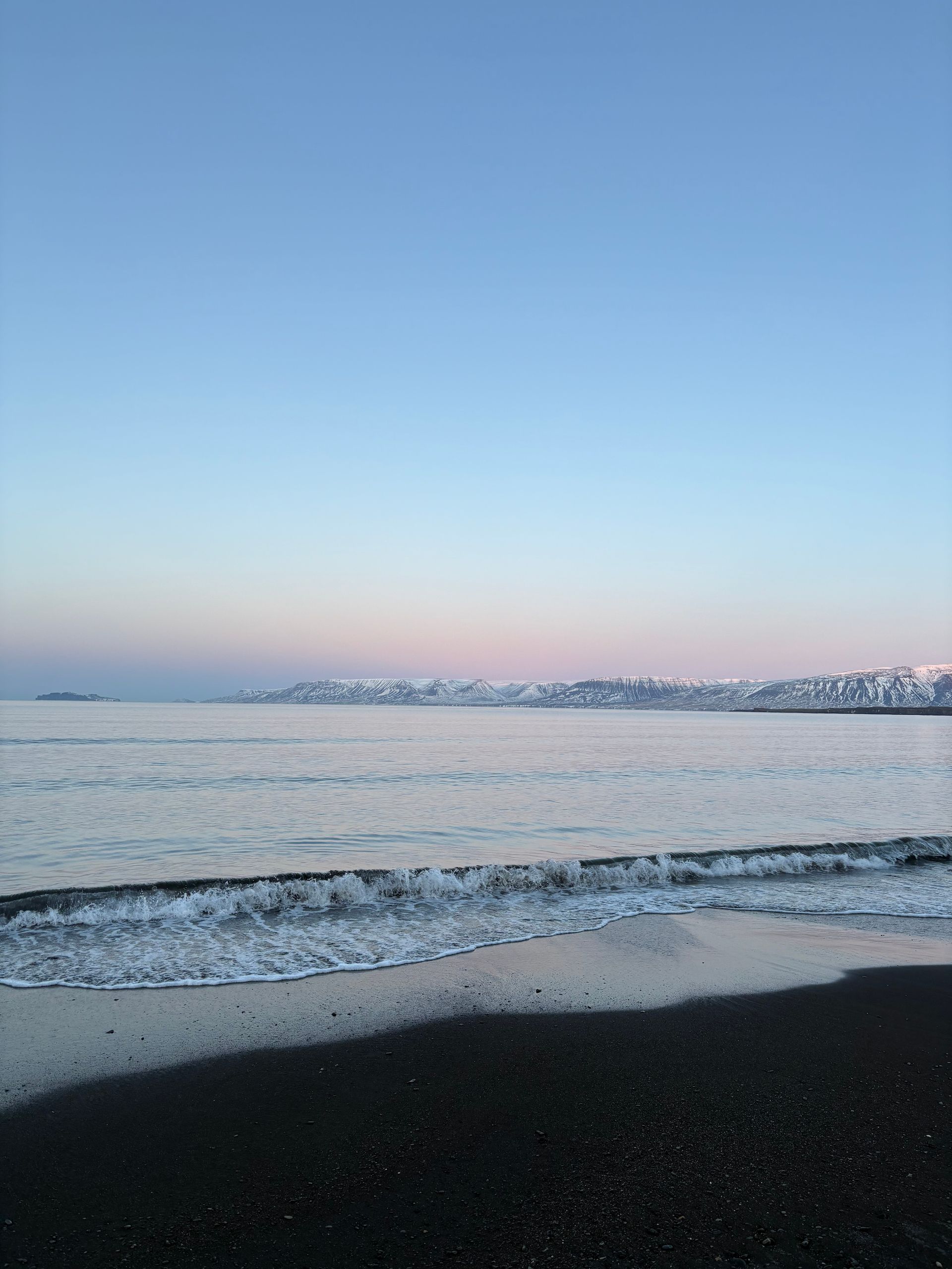Dark Skagafjörður shoreline with calm water and snowy mountains across the fjord.