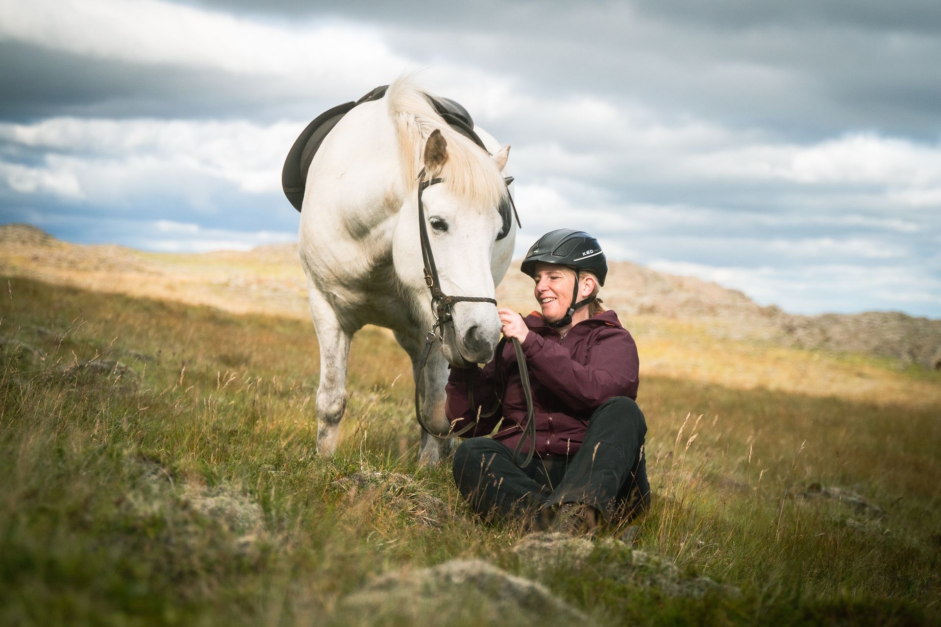 Traveler sitting beside an Icelandic horse in open Skagafjörður countryside.