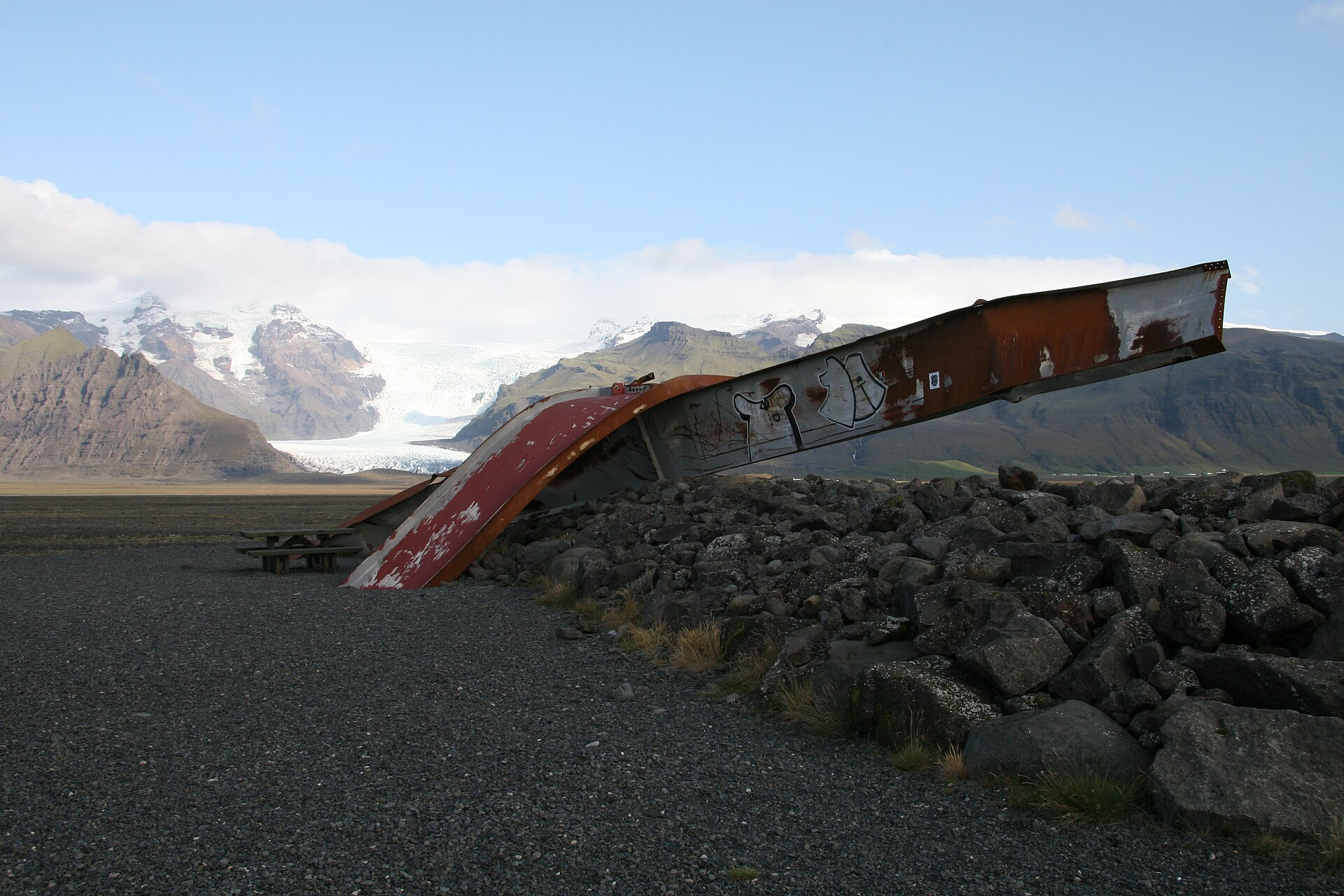 Twisted red steel from the old Skeiðará bridge displayed on the black sand with Vatnajökull in the background.