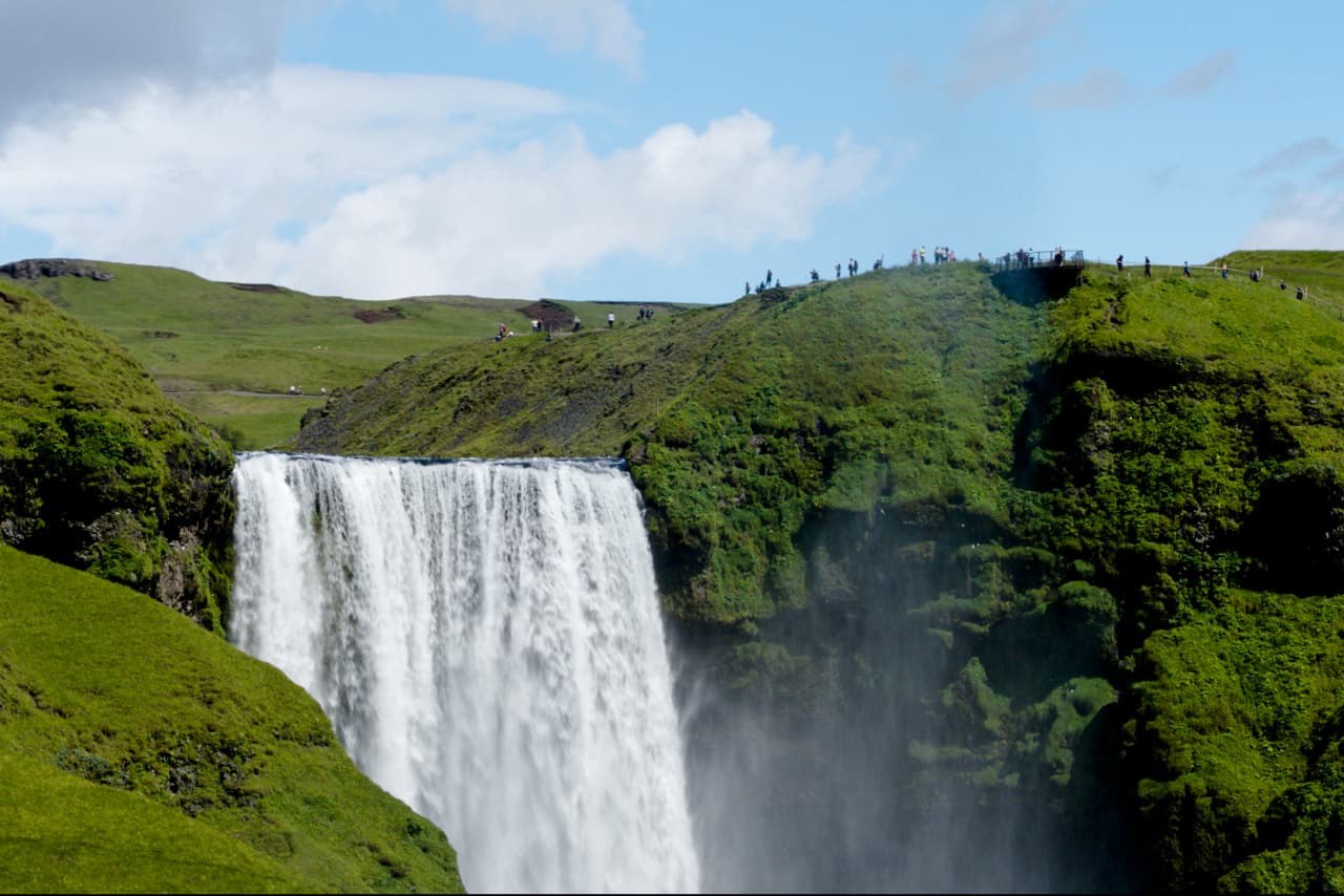View over Skogafoss from above with the waterfall dropping toward the coastal plain.