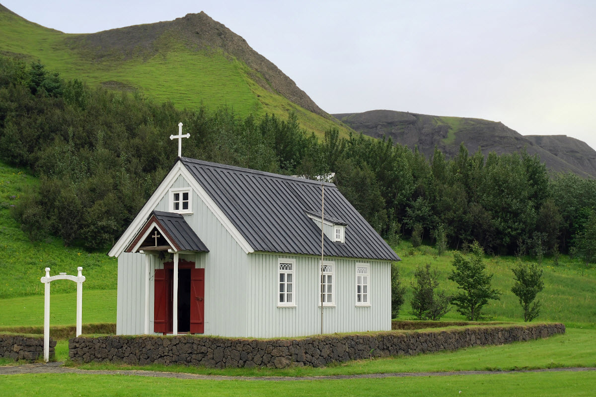 White Skógar church below green hills and trees in South Iceland.