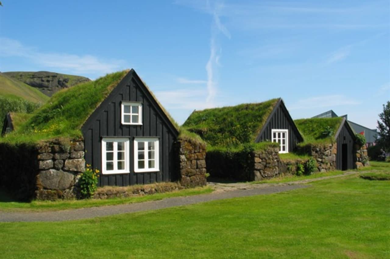 Turf-roofed houses at Skógar Museum below green South Iceland hills.