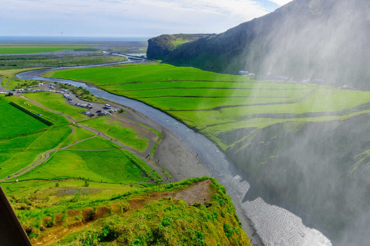 View from above Skógafoss toward the green fields and parking area around Skógar.