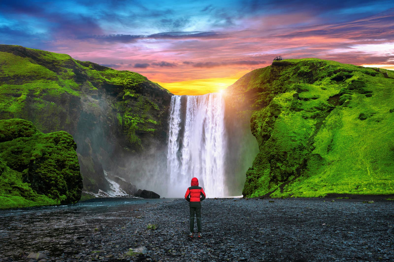 Visitor near the base of Skógafoss with the waterfall dropping from green cliffs at Skógar.