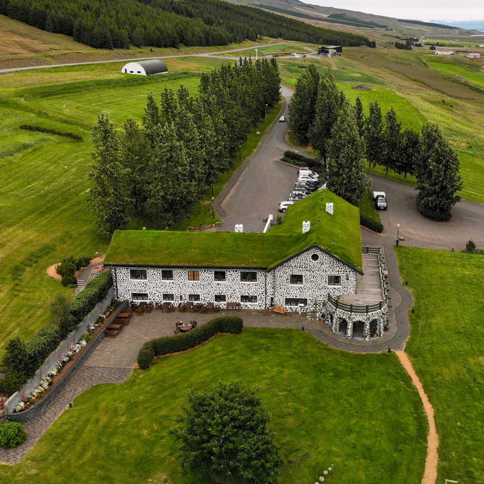 Aerial view of Gunnarshús at Skriðuklaustur with parking, trees, fields, and Fljótsdalur slopes around the cultural site.