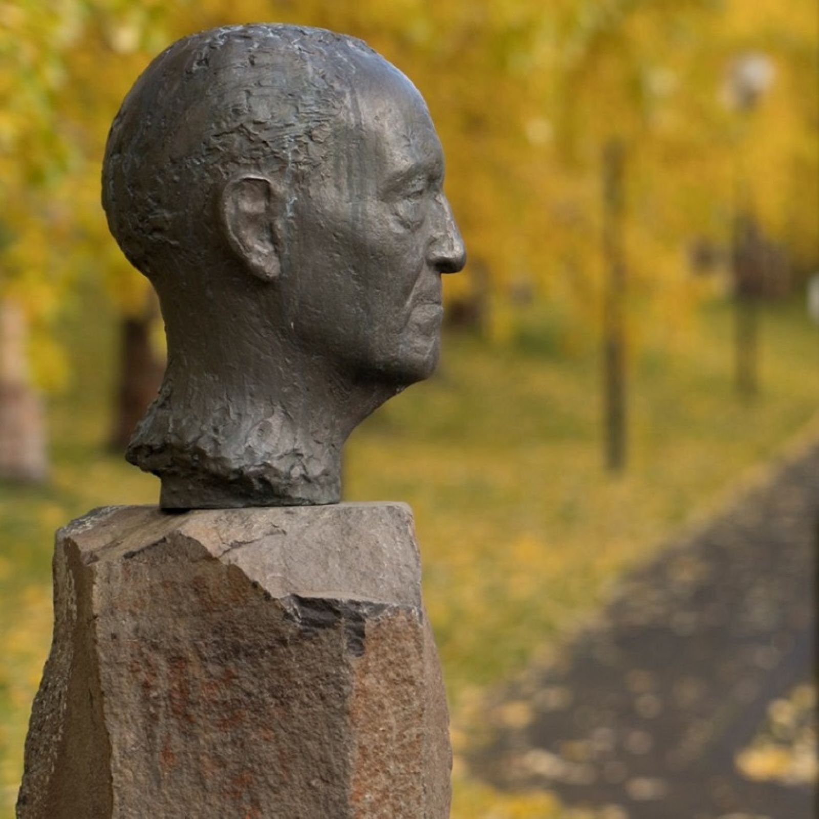 Bronze bust of Gunnar Gunnarsson outside Skriðuklaustur with autumn trees and a path behind it.