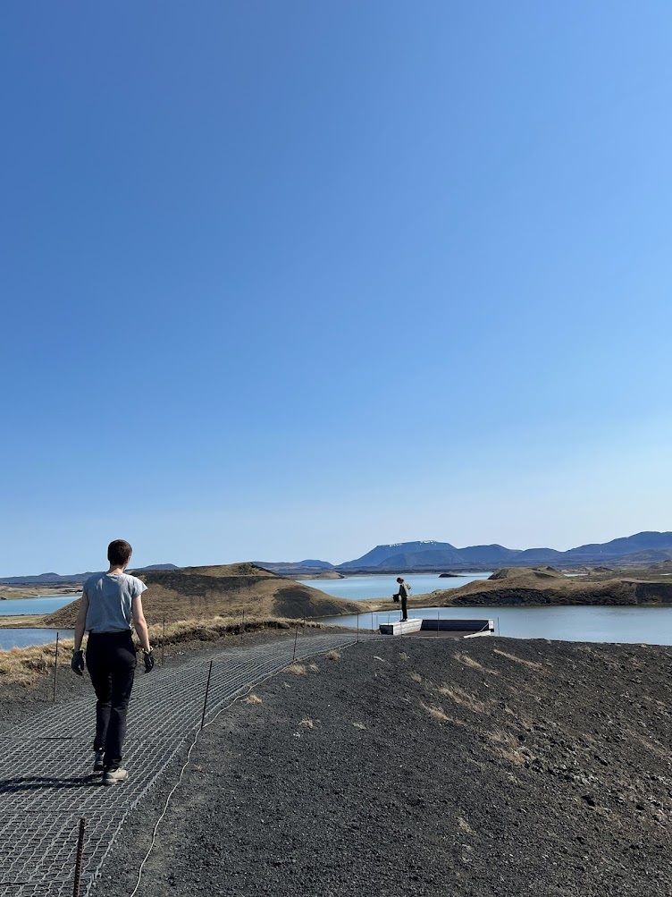 Visitors walking on a marked Skútustaðagígar crater rim path with Lake Mývatn and low hills behind them.