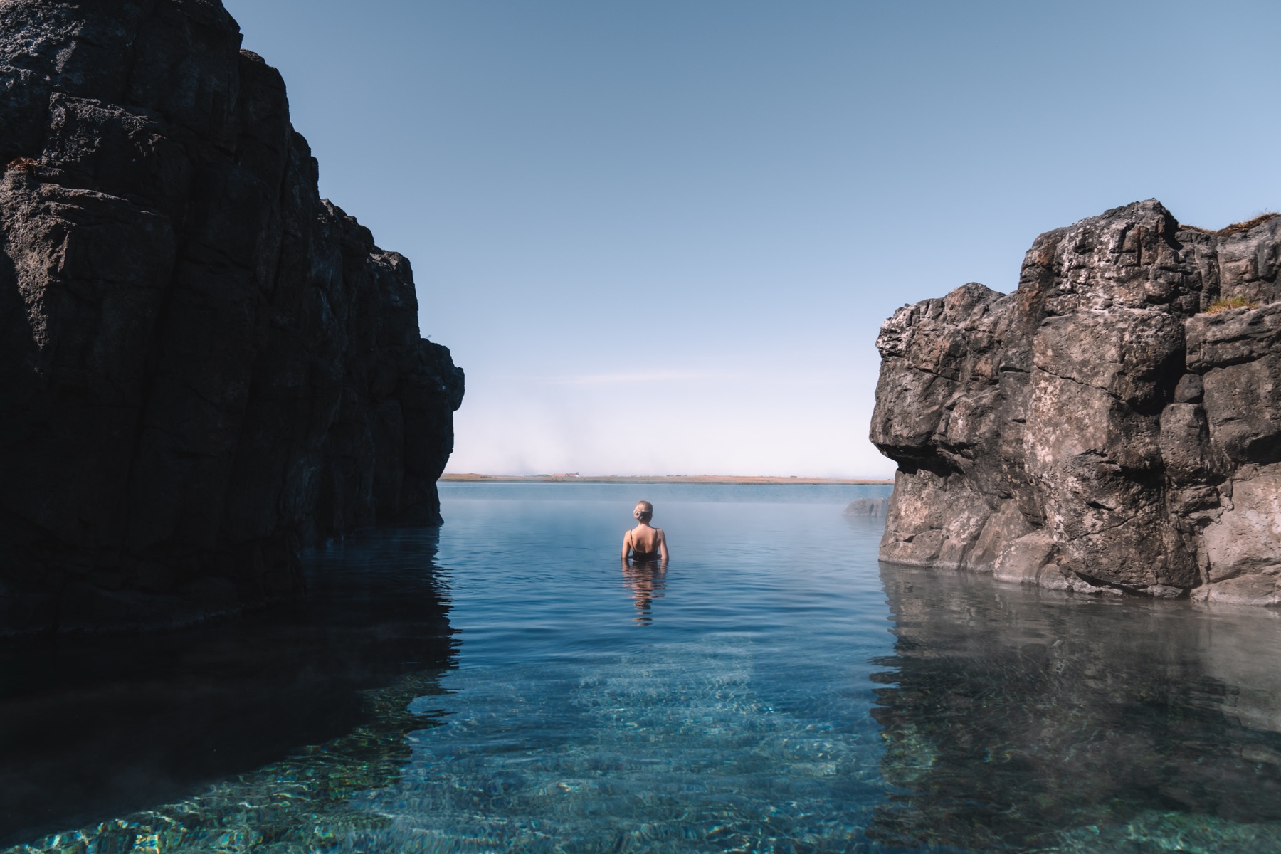 Sky Lagoon rock wall and infinity-edge water with one bather facing the ocean outside Reykjavík.