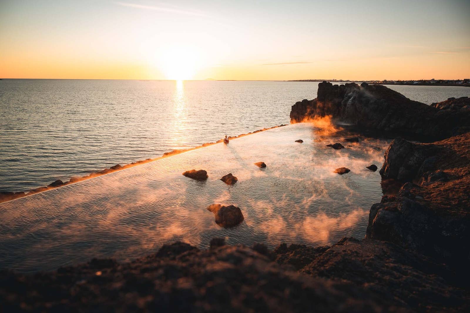 Sky Lagoon infinity edge glowing at sunset with steam rising above the water and the North Atlantic beyond.