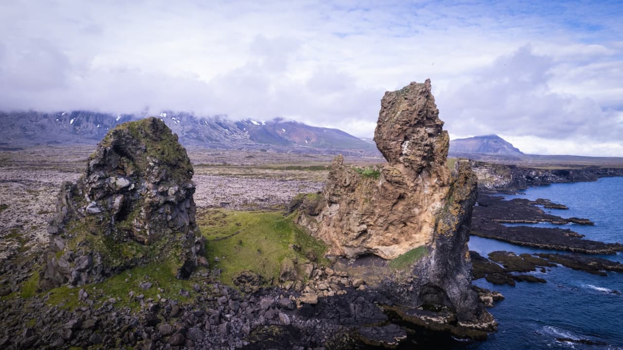 Lóndrangar sea stacks with Snæfellsjökull clouded in the background above the lava coast.